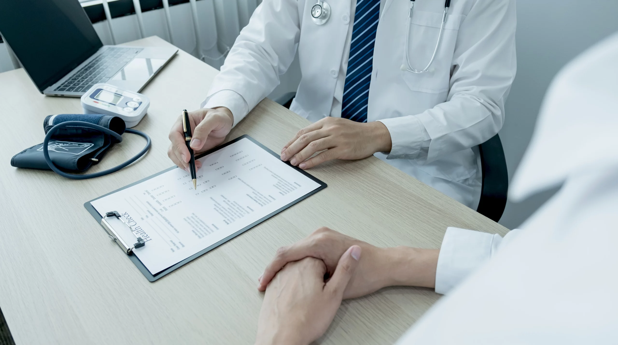 Doctor in white coat discusses form with patient at kitchen‑table, blood pressure monitor and laptop visible — illustrating when to seek a second opinion in a Missouri workers’ comp case.